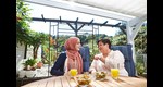 Zwei Frauen sitzen am Tisch und unterhalten sich, eine trägt ein Kopftuch.