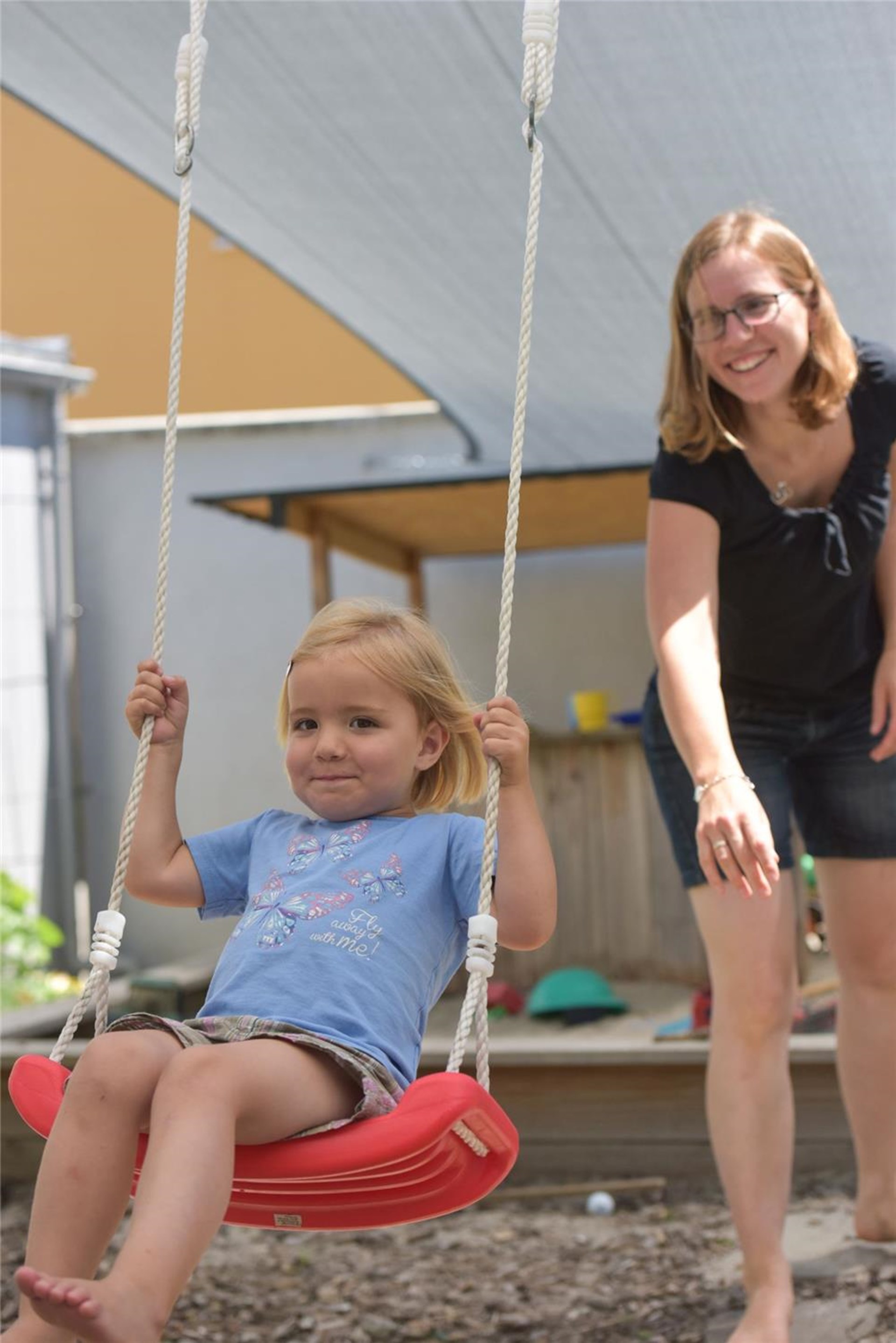 Eine Mutter schubst ihre Tochter auf der Schaukel an